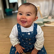 Mya a rejoint le concours — aidez-le/la à gagner de superbes lots ! baby, child, smiling, sitting, blue_overall, white_shirt, indoor, wooden_floor, toy_ball, happy, rosy_cheeks, face, person, cute, young_child, portrait, home, blurred_background, playful, infant
