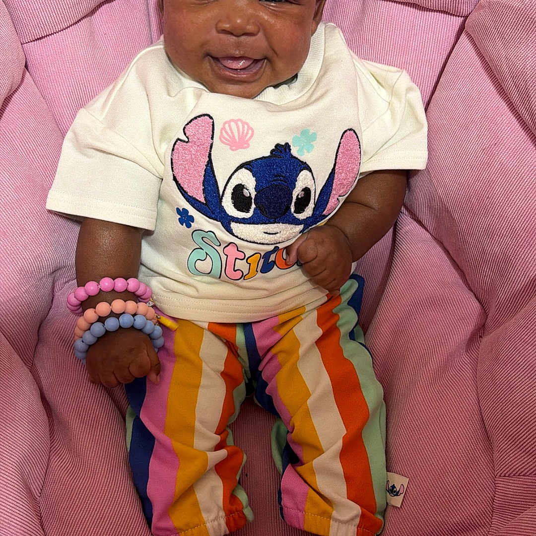 Delilah Dior Moore joined the competition — help win amazing prizes! baby, child, smiling, sitting, colorful_clothing, headband, bracelets, pink_cushion, tshirt, striped_pants, indoor, happy, cute, accessories, infant, portrait, person, fashion, comfortable, young
