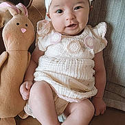 Sloane joined the competition — help win amazing prizes! baby, child, plush_toy, bunny, headband, smile, sitting, dress, indoor, childhood, cute, toy, young_child, person, furniture, cozy, portrait, happy, infant, cuddly