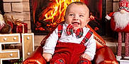 Aylan participe au concours pour gagner de l'argent avec cette photo : baby, child, fireplace, christmas, holiday, red_clothing, plaid, armchair, smiling, toy, reindeer_toy, decorations, cozy, festive, indoor, carpet, warmth, cute, cheerful, portrait