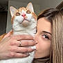 cat, woman, indoor, affection, pet, orange_cat, white_cat, kiss, close_up, human_hand, portrait, love, domestic_animal, feline, face, holding, whiskers, brown_hair, necklace, turtleneck