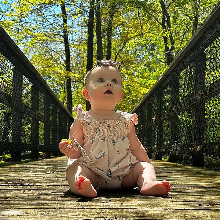 Adalee joined the competition — help win amazing prizes! baby, dress, fawn, fence, flooring, foot, grass, happy, human_leg, leisure, natural_environment, people_in_nature, plant, recreation, sitting, sunlight, toddler, toy, tree, wood