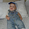 John is registered to the contest to win money with this photo: baby, child, smiling, cap, overalls, sneakers, nike, bed, pillow, clothing, happy, person, footwear, casual, cute, infant, portrait, indoors, relaxing, comfortable