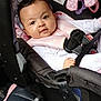 baby, infant, car_seat, straps, safety, plush_toy, curly_hair, clothing, seat, child, car_interior, cute, face, person, indoors, smiling, pink, black, comfort, young