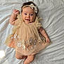 baby, infant, smile, dress, headband, flower, embroidery, lying_down, happy, cute, child, soft_light, fabric, bed, skin, portrait, person, indoors, adorable, young_child
