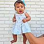 Isabella is registered to the contest to win money with this photo: baby, child, infant, dress, blue_bow, headband, white_brick_wall, arm, hand, barefoot, curious_expression, holding, person, cute, outdoor, skin, smiling, young_child, portrait, summer_clothing