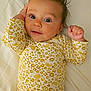 Isabella joined the competition — help win amazing prizes! baby, infant, child, onesie, yellow, floral_pattern, spiky_hair, lying_down, bed, white_sheet, cute, curious, hand, face, portrait, indoors, skin, expression, small_fingers, young