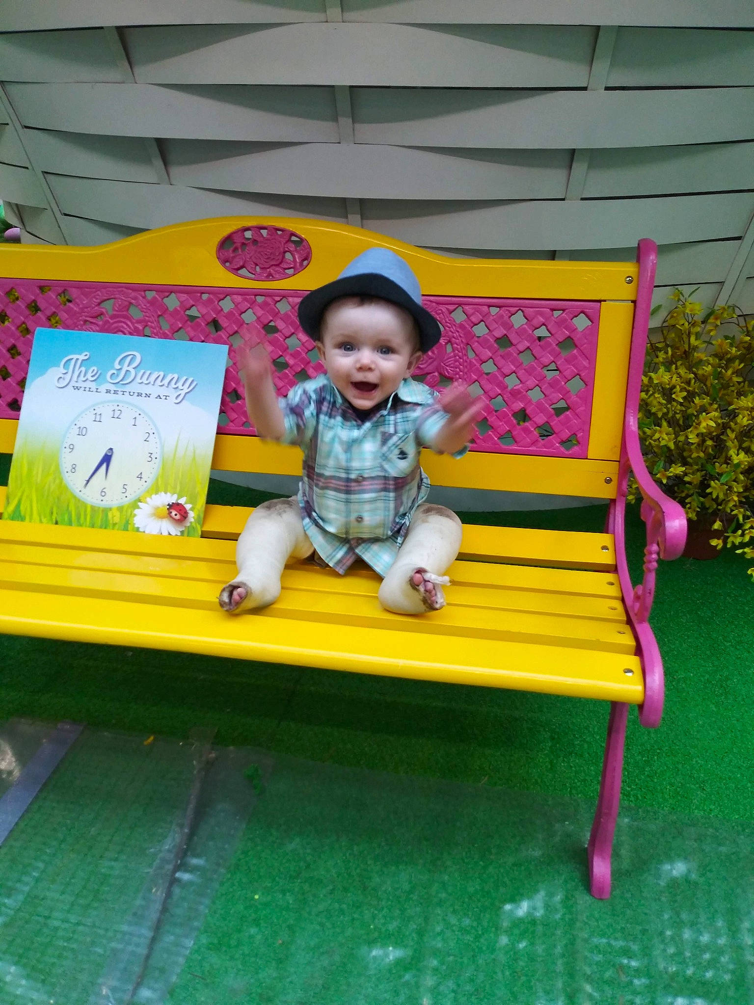 Johnny is registered to the contest to win money with this photo: baby, chair, child, city, fun, grass, hat, leisure, magenta, outdoor_furniture, person, plant, play, recreation, shorts, sitting, smile, tire, toddler, wheel