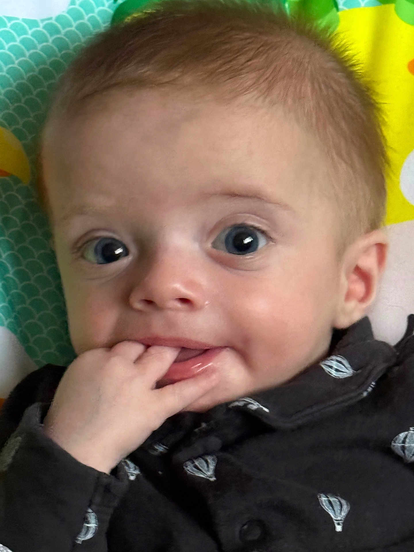 Theodore is registered to the contest to win money with this photo: baby, infant, face, blue_eyes, hand, fingers, clothing, pattern, hot_air_balloon, curious, closeup, portrait, child, cute, young, skin, mouth, expression, background, colorful