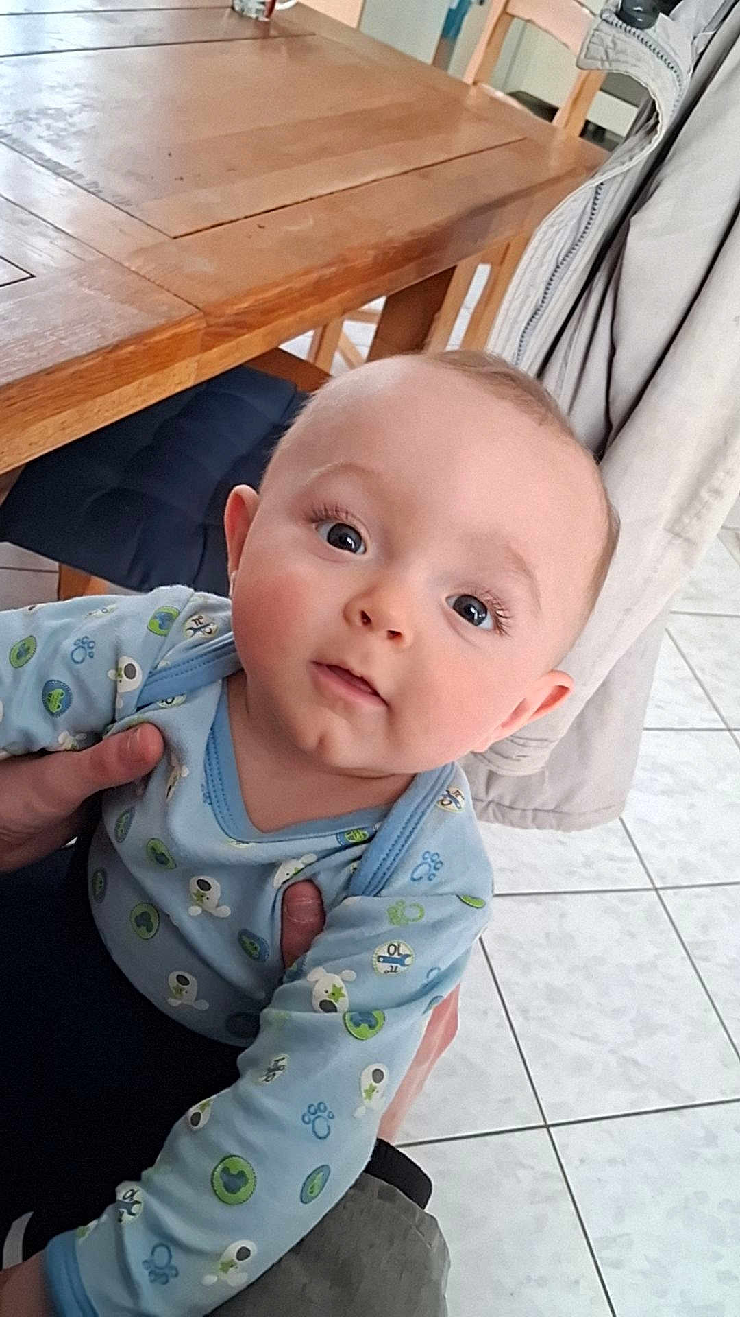 Eythan a rejoint le concours — aidez-le/la à gagner de superbes lots ! baby, child, infant, person, face, blue_clothing, long_sleeves, hand, wooden_table, chair, tile_floor, indoor, curious, holding, cute, eyelashes, rosy_cheeks, looking_at_camera, casual, home