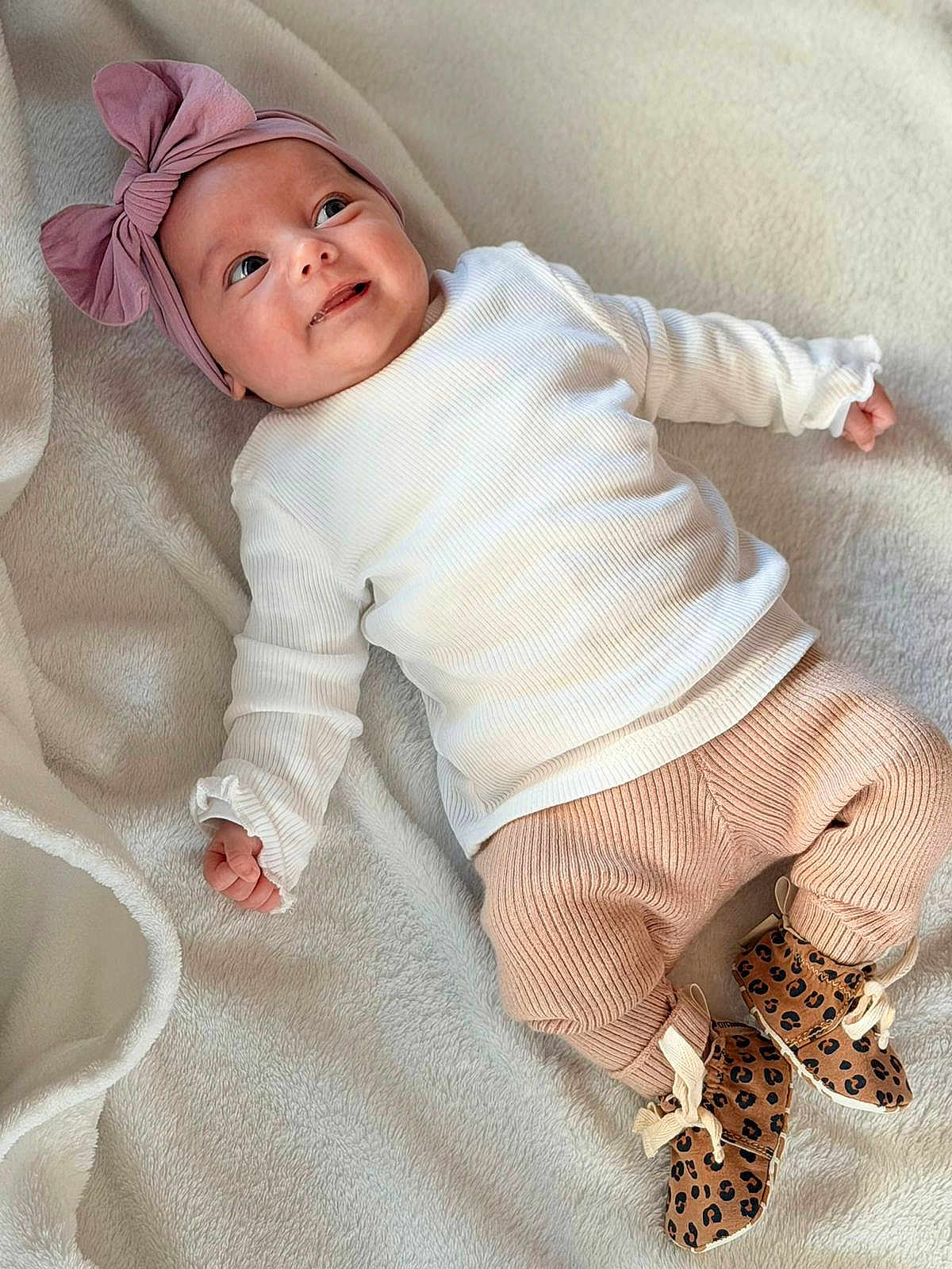 Camélia participe au concours pour gagner de l'argent avec cette photo : baby, infant, child, headband, bow, white_shirt, ribbed_clothing, pants, peach_color, leopard_print, booties, blanket, soft_texture, smiling, lying_down, cute, portrait, indoors, happy, person