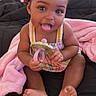 baby, child, smiling, cute, toy, blanket, pink_blanket, black_blanket, hair_buns, sitting, indoors, happy, tongue_out, colorful_clothing, barefoot, infant, portrait, playful, young_child, person