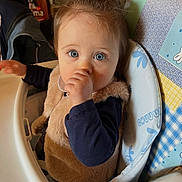 Louise a rejoint le concours — aidez-le/la à gagner de superbes lots ! baby, infant, child, high_chair, thumb_sucking, blue_eyes, fuzzy_vest, ponytail, bib, tray, patterned_fabric, indoor, jacket, backpack, dining_area, face, portrait, close_up, curious, seated