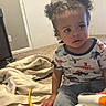 Ke-Von is registered to the contest to win money with this photo: toddler, child, curly_hair, dinosaur_shirt, indoor, carpet, blanket, toy, yellow_dinosaur, casual_clothing, shorts, curious_expression, young_child, home, floor, sitting, person, playtime, room, light