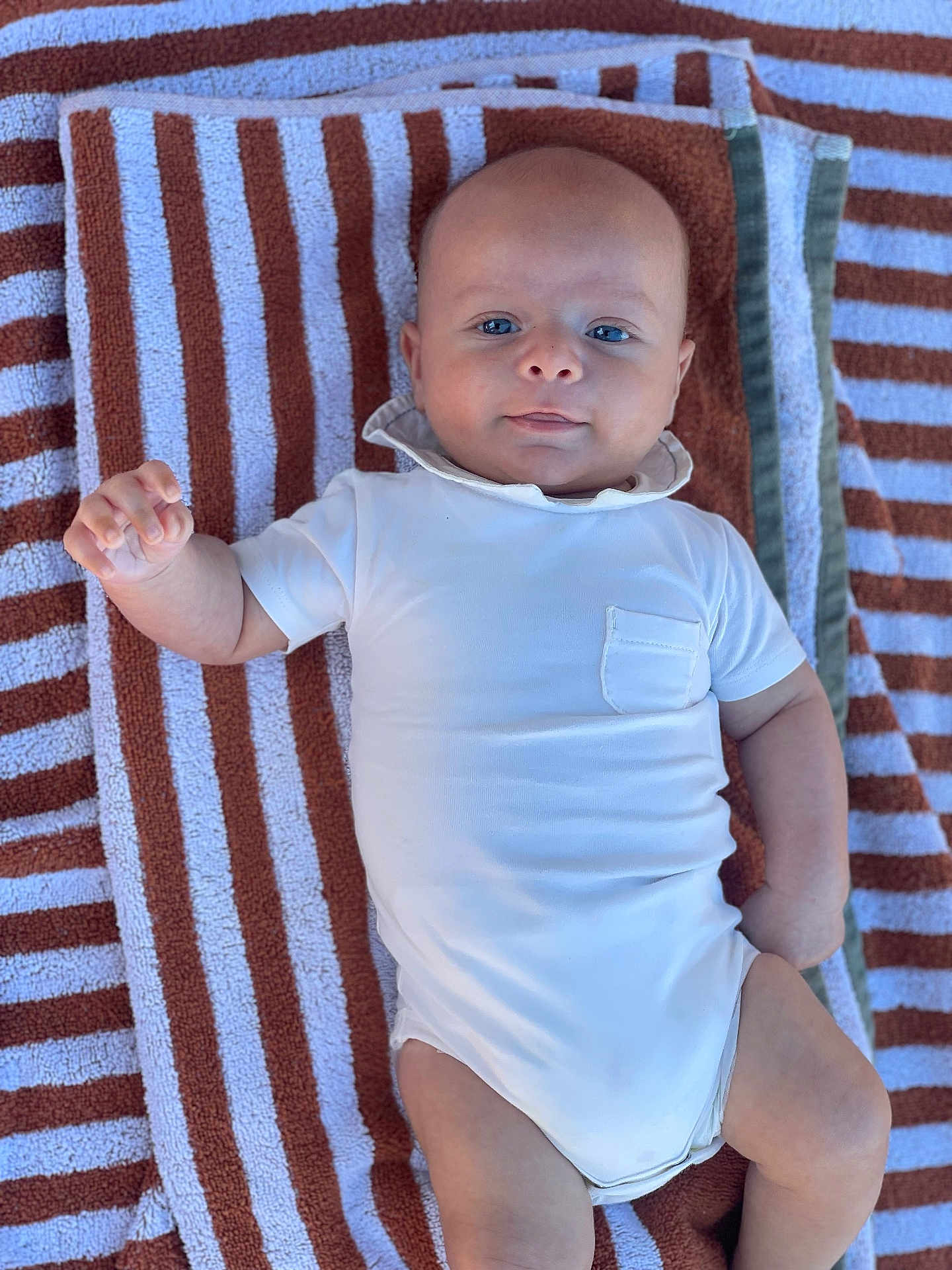 Livio participe au concours pour gagner de l'argent avec cette photo : baby, infant, towel, striped_towel, white_onesie, clothing, blue_eyes, cute, laying_down, portrait, child, skin, hand, face, head, soft_light, relaxed, casual, summer, outdoor