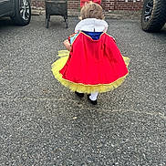 Drue joined the competition — help win amazing prizes! toddler, child, costume, snow_white, red_bow, yellow_tutu, walking, asphalt, stroller, brick_wall, car, tire, outdoor, back_view, curly_hair, cape, sidewalk, vehicle, parking_lot, playful