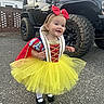 Drue is registered to the contest to win money with this photo: toddler, child, costume, dress, yellow_tutu, red_bow, smile, outdoor, driveway, vehicle, jeep, tire, black_vehicle, face, person, sidewalk, happy, clothing, headband, footwear
