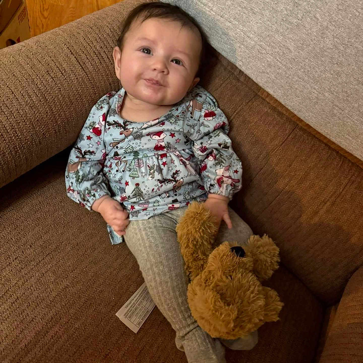 Kenzie Lynn joined the competition — help win amazing prizes! baby, brown_couch, child, couch, cozy, cute, furniture, happy, home, indoor, infant, pajamas, person, plush_toy, relaxing, sitting, smile, soft_toy, teddy_bear, wood_floor