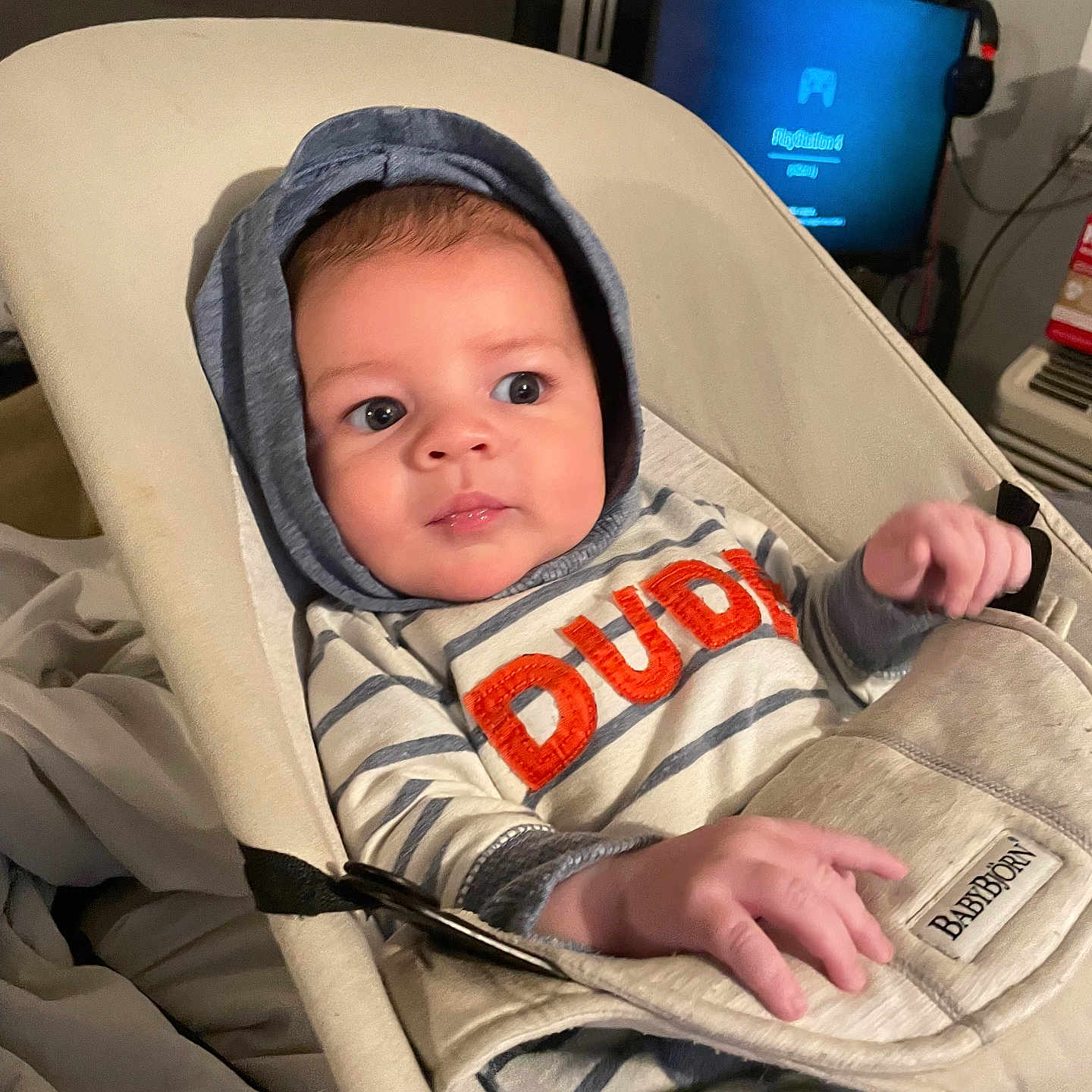 Xaidynn joined the competition — help win amazing prizes! baby, baby_rocker, blanket, casual, child, comfort, curious_expression, electronics, face, furniture, hands, headwear, hoodie, indoor, infant, person, seated, striped_clothing, television, young_child