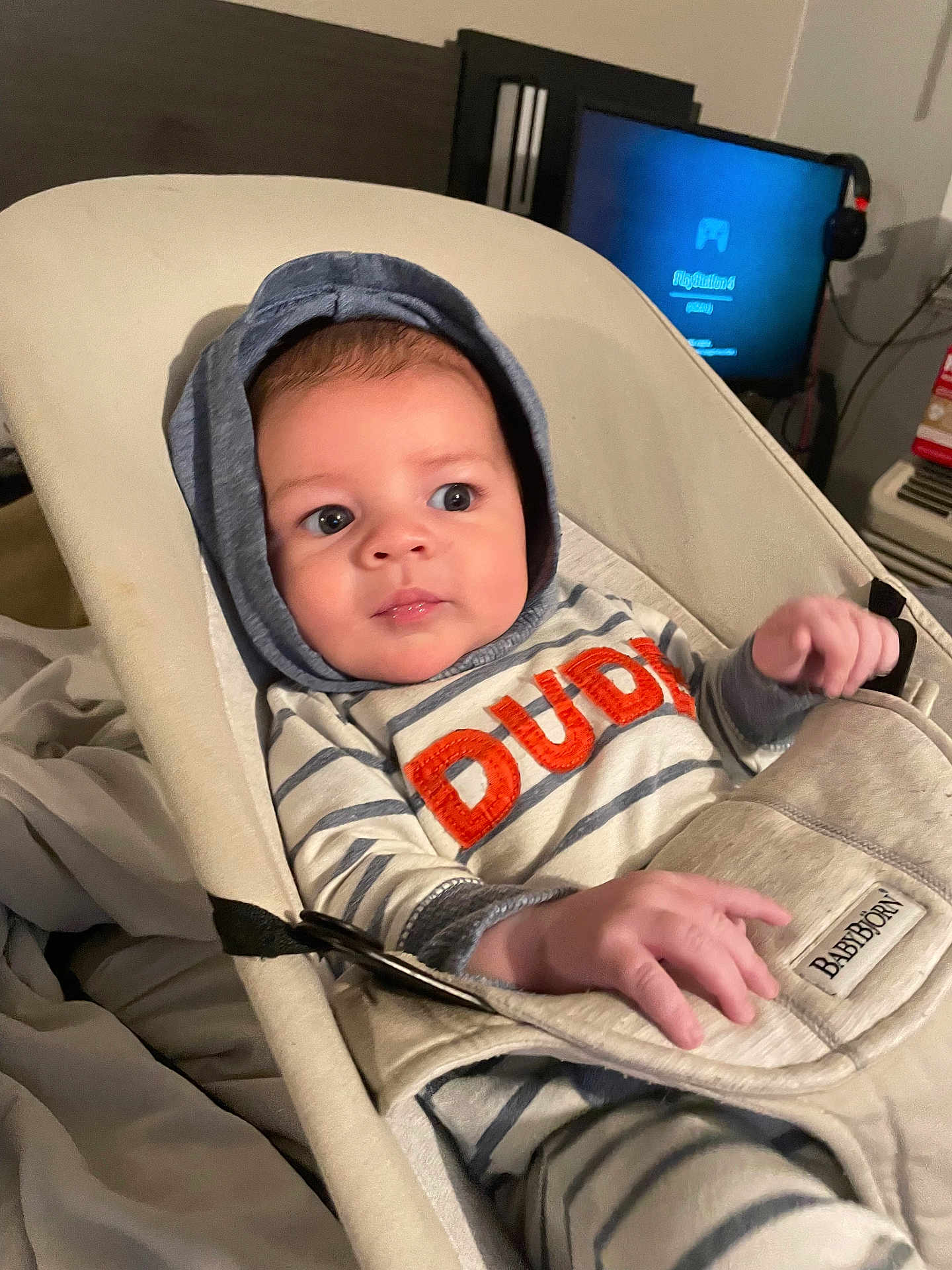 Xaidynn joined the competition — help win amazing prizes! baby, baby_rocker, blanket, casual, child, comfort, curious_expression, electronics, face, furniture, hands, headwear, hoodie, indoor, infant, person, seated, striped_clothing, television, young_child