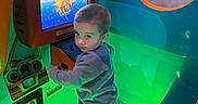 Mylin is registered to the contest to win money with this photo: amusement, arcade, child, clothing, colorful, curious, entertainment, game, green_light, indoor, neon_light, pants, play, reflection, screen, sneakers, standing, submarine, toddler, toy