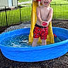 bare_chest, blue_pool, boy, child, daytime, fence, fun, grass, happy, outdoor, play, red_swim_trunks, slide, splash, summer, swimming_pool, toy, water, water_play, yellow_slide