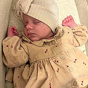 Anelya participe au concours pour gagner de l'argent avec cette photo : baby, sleeping, infant, hat, dress, beige, floral_pattern, crib, cushion, peaceful, closeup, child, newborn, soft_lighting, cozy, small_hands, buttoned_dress, portrait, indoors, resting