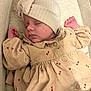 baby, sleeping, infant, hat, dress, beige, floral_pattern, crib, cushion, peaceful, closeup, child, newborn, soft_lighting, cozy, small_hands, buttoned_dress, portrait, indoors, resting