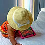 toddler, straw_hat, tablet, bed, orange_clothing, child, indoor, curtains, quilted_bedspread, hand, technology, play, white_bow, colorful, furniture, lamp, relaxation, screen, patterned_clothing, room