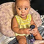baby, bed, braids, child, curious, cute, expression, face, hands, home, indoor, legs, pacifier, person, pillow, plush_toy, remote_control, sitting, skin, yellow_clothing