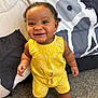 baby, bed, blanket, bright_clothing, carpet, child, curly_hair, cute, earrings, expression, face, happy, indoors, pattern, person, smiling, standing, toddler, yellow_outfit, young_child