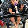 baby, black_shirt, child, cute, expression, face, feet, floor, grocery_store, hands, indoor, infant, looking_up, pacifier, person, plastic_cart, shopping_cart, sitting, toy, white_bow