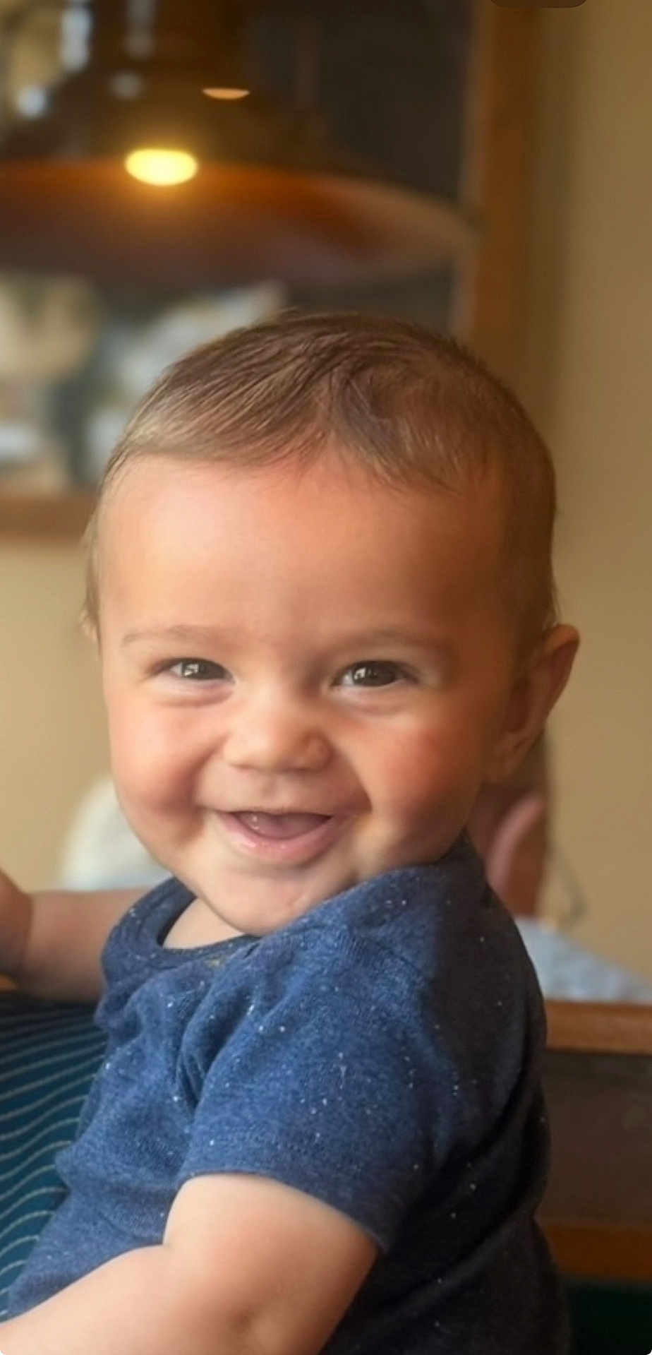 David is registered to the contest to win money with this photo: baby, smiling, child, indoor, blue_shirt, cute, portrait, happy, face, young_child, infant, person, light, blurred_background, closeup, skin, hair, seated, toddler, expression