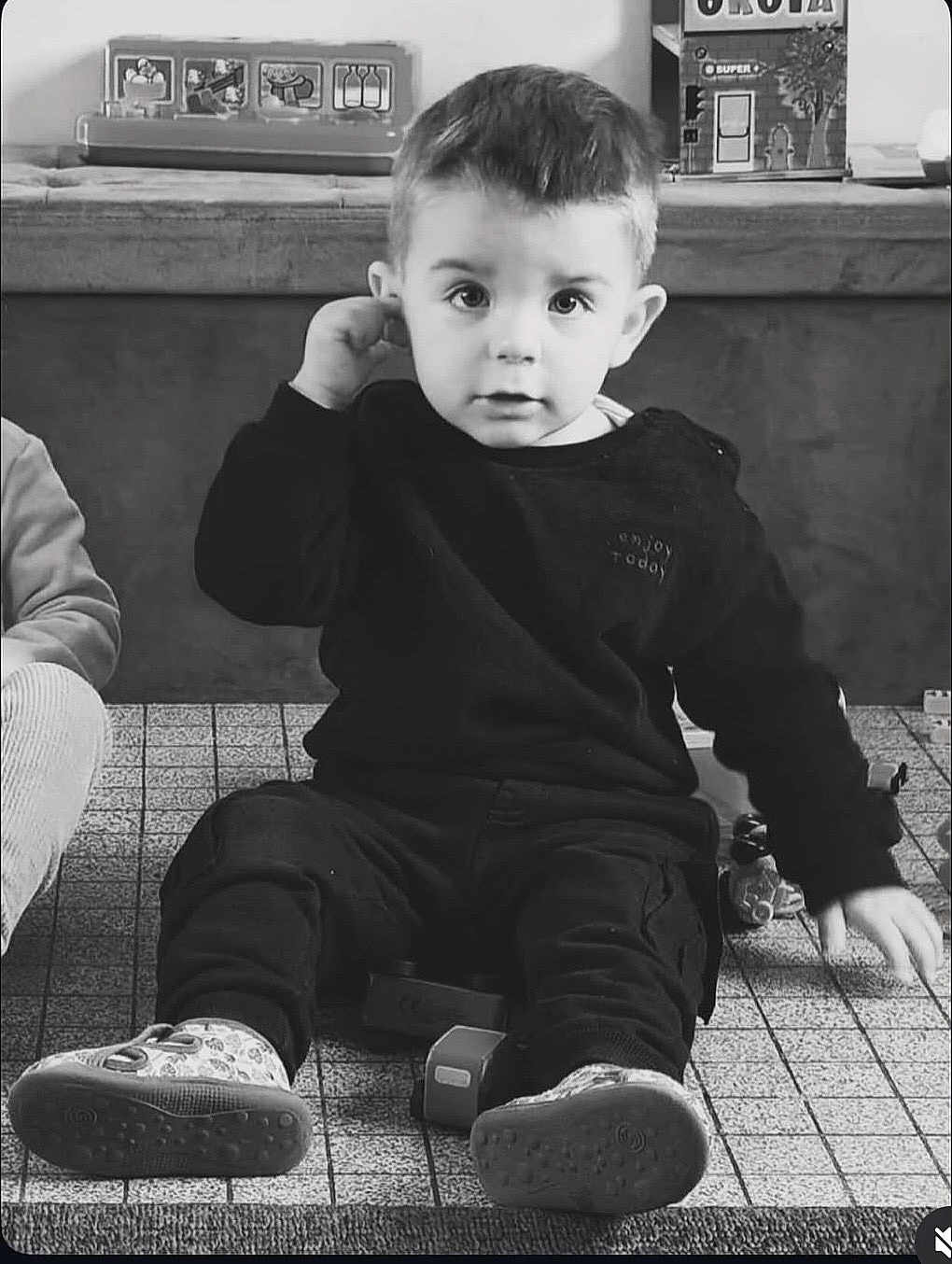 Malo participe au concours pour gagner de l'argent avec cette photo : child, toddler, sitting, indoor, black_and_white, toy, curious, portrait, eyes, short_hair, ear, sneakers, floor_tiles, carpet, sweatshirt, pants, playroom, bench, blocks, cute