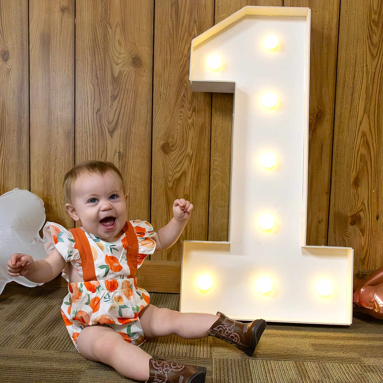 Luna is registered to the contest to win money with this photo: baby, boot, clothing, face, footwear, hardwood, head, indoors, interiordesign, lighting, number, pants, person, photography, portrait, shoe, sitting, symbol, text, wood