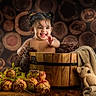 baby, blanket, child, cozy, cute, decor, flowers, happy, indoor, infant, knitted_toy, natural_background, pigtails, playful, portrait, smiling, teddy_bear, warm_lighting, wood_logs, wooden_bucket