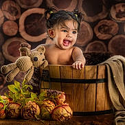 Sitara joined the competition — help win amazing prizes! toddler, child, baby, wooden_bucket, toy, crocheted_teddy, flowers, pigtails, smiling, happy, portrait, indoor, decorative, blanket, wood_background, cute, playful, young_child, warm_lighting, cozy