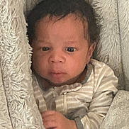 Daniel is registered to the contest to win money with this photo: baby, infant, blanket, clothing, face, hand, person, portrait, indoor, cute, newborn, soft, cozy, sleepwear, striped, young_child, fur_texture, warm, expression, comfort