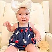 Blakely joined the competition — help win amazing prizes! baby, child, smile, headband, bow, dress, patterned_clothing, sitting, chair, cushion, milestone_marker, wooden_sign, indoor, happy, cute, infant, ten_months, person, portrait, light_background