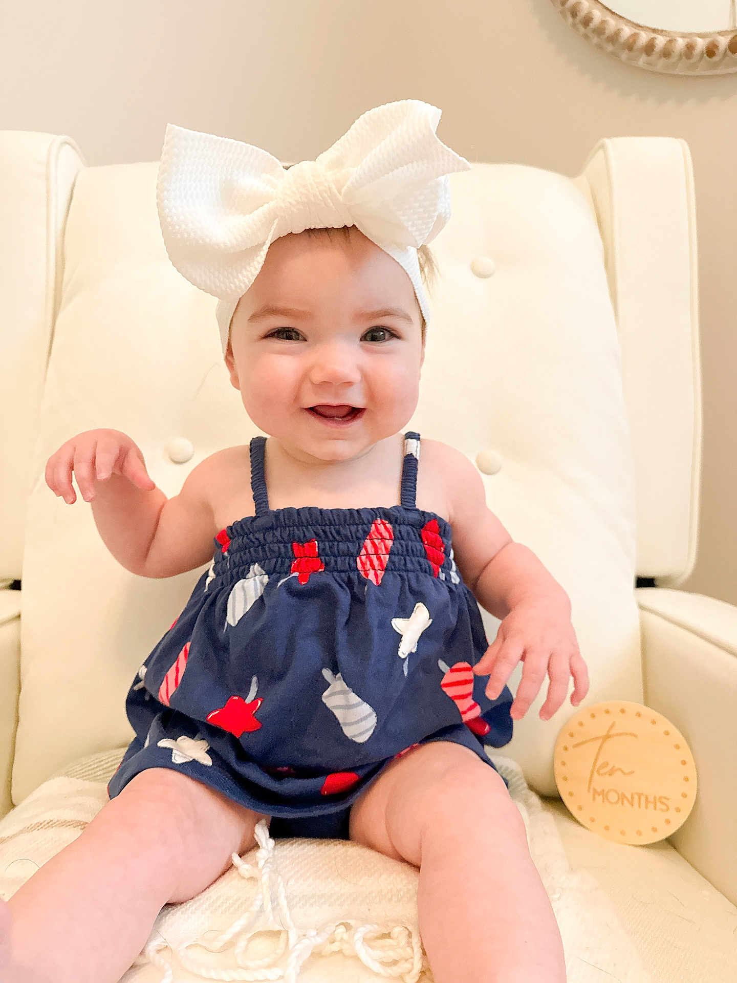 Blakely joined the competition — help win amazing prizes! baby, child, smile, headband, bow, dress, patterned_clothing, sitting, chair, cushion, milestone_marker, wooden_sign, indoor, happy, cute, infant, ten_months, person, portrait, light_background