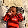 baby, infant, onesie, striped_clothing, red_clothing, navy_clothing, face, hair, hand, fist, changing_pad, quilt, blanket, bed, lying_down, newborn, person, indoor, cute, portrait