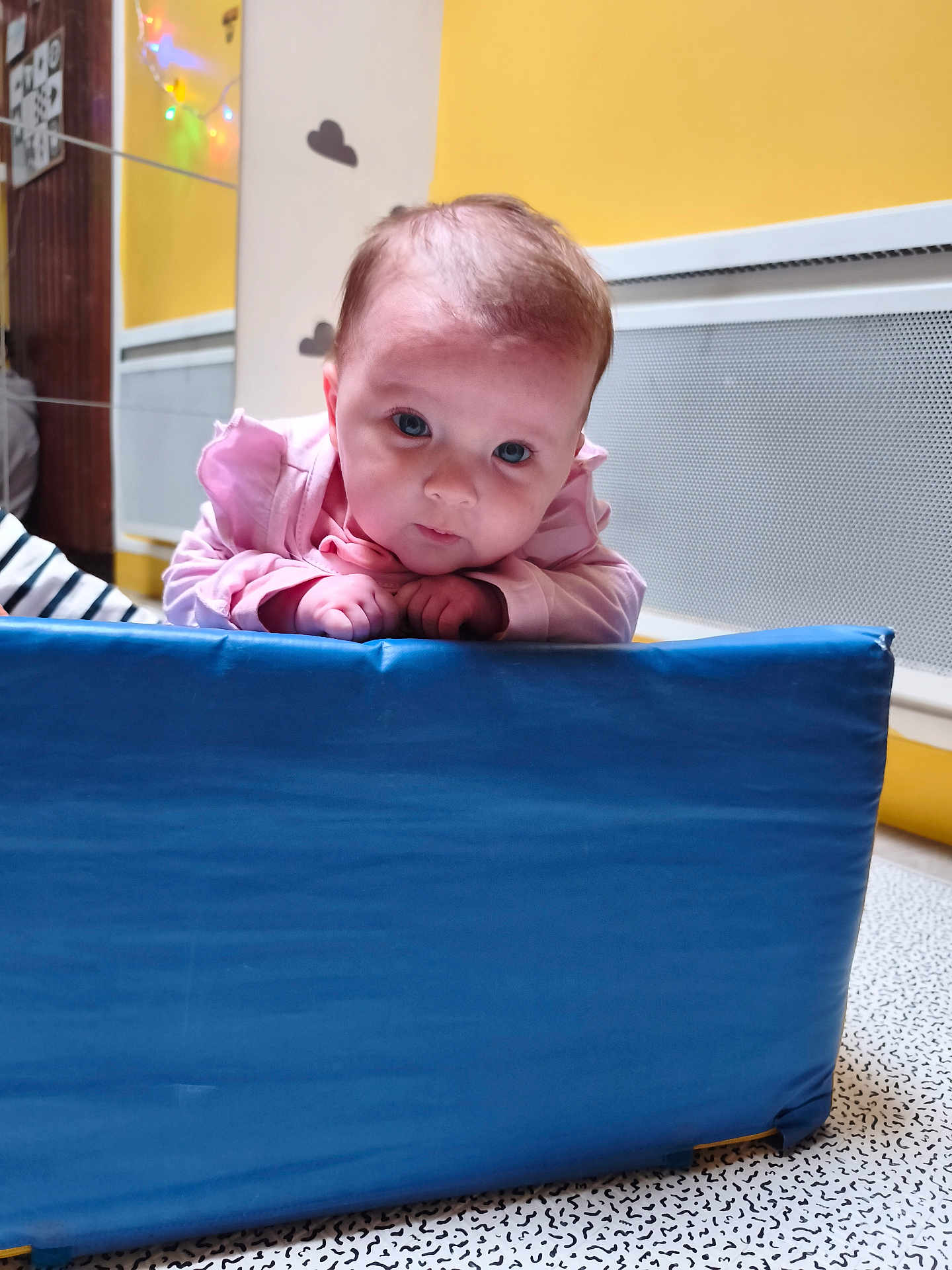 Kamelya participe au concours pour gagner de l'argent avec cette photo : baby, infant, pink_clothing, blue_mat, indoor, child, face, hands, floor, wall, yellow_wall, decorations, cloud_stickers, curious, looking, young_child, head, expression, cute, soft_lighting