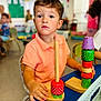 child, boy, toy, wooden_toy, stacking, classroom, education, table, colorful, polo_shirt, focus, play, learning, indoor, preschool, young_child, seat, hand, curious, background