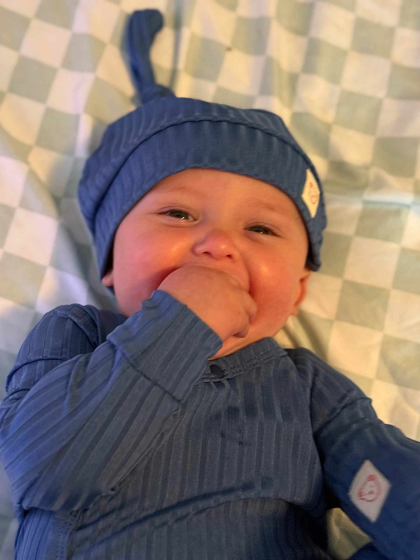 Bentley joined the competition — help win amazing prizes! baby, infant, blue_clothing, hat, hand_in_mouth, blanket, checkered_pattern, cute, child, smiling, lying_down, face, skin, one_person, indoors, soft_lighting, close_up, portrait, happy, young_child