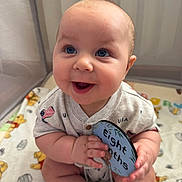 Liam is registered to the contest to win money with this photo: baby, infant, eight_months, smiling, blue_eyes, milestone_card, blanket, playpen, cute, happy, sitting, clothing, usa_flag, chubby_cheeks, hands, portrait, indoor, child, person, milestone