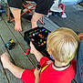Tony is registered to the contest to win money with this photo: child, blonde_hair, red_clothing, toy_cars, black_organizer, wooden_floor, barefoot, folding_chair, adult, playtime, porch, deck, casual, sitting, floor, collection, miniature_toys, person, indoor, relaxed