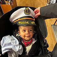 Jarod a rejoint le concours — aidez-le/la à gagner de superbes lots ! blanket, captain_hat, child, clothing, cozy, cute, face, hand, indoor, jacket, person, portrait, red_scarf, smile, stroller, swords, toddler, toy_store, wooden_floor, young_child