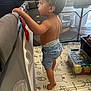 barefoot, child, computer, curious, diaper, floor_mat, home, indoor, light, mesh, plastic_box, playpen, profile, shorts, standing, tiptoes, toddler, toys, window, young_child
