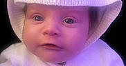 Genesis is registered to the contest to win money with this photo: baby, child, cozy, cute, dark_background, expression, eyes, face, hand, indoor, infant, knit_hat, knitwear, newborn, portrait, purple_tint, soft_lighting, sweater, warmth, white_clothing