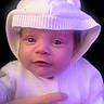 Genesis is registered to the contest to win money with this photo: baby, infant, child, knit_hat, white_clothing, cute, hand, portrait, face, eyes, soft_lighting, purple_tint, warmth, cozy, sweater, knitwear, newborn, expression, indoor, dark_background